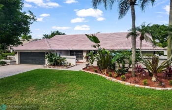 A beautifully paved driveway leads to an inviting front entrance, framed by lush, tropical landscaping and mature trees that provide both privacy and a touch of nature's tranquility.