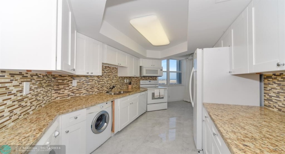 Spacious kitchen with white cabinets and appliances and washer and dryer located in unit
