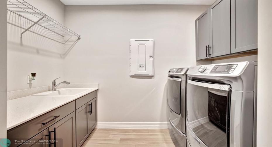 Laundry room with sink and elevated washer and dryer, Smart home central panel on wall.