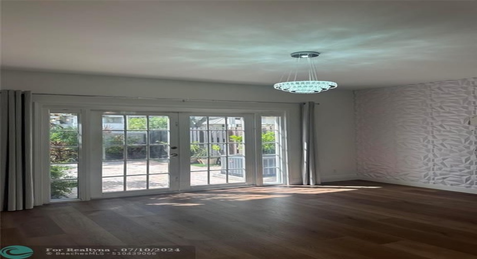 Impact French Doors With Side Lights And Complimenting Drapes, Tiled Wall For Your Large Screen TV, Contemporary Lighting Fixture With Contiguous Wood Like Engineered Flooring Throughout This Townhome.