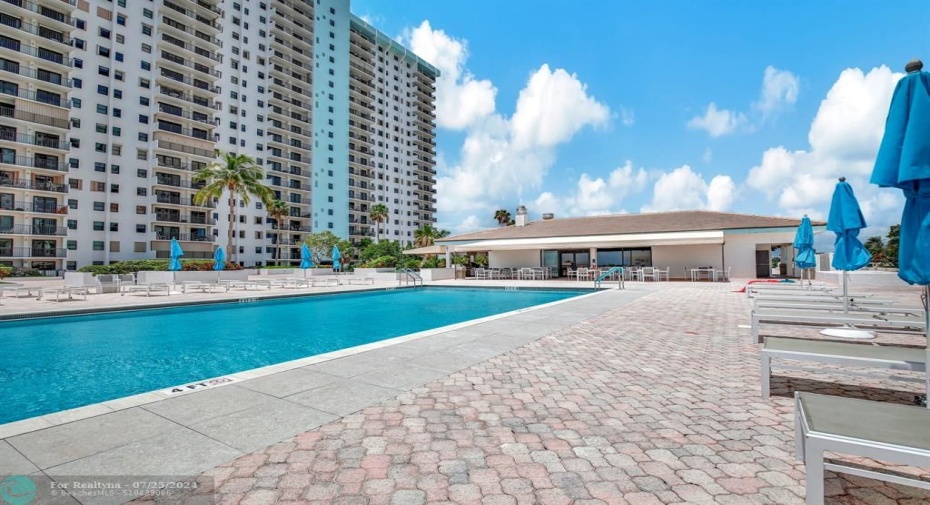 Enormous pool deck that overlooks both the ocean and the intracoastal with two heated pools, loungers, umbrellas and onsite restaurant in the center.