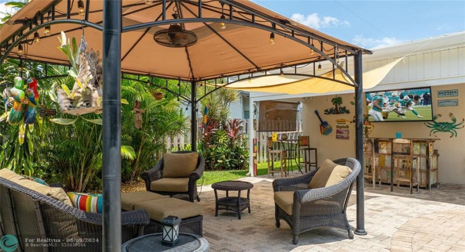 Gazebo sits next to covered area set up as TV, bar space