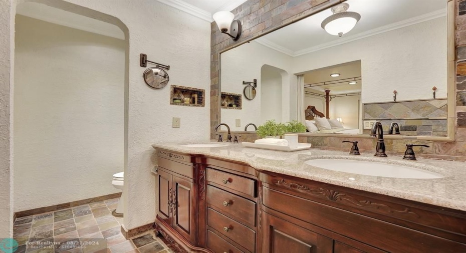 Renovated European style primary bathroom with dual sinks, wood cabs, slate flooring.