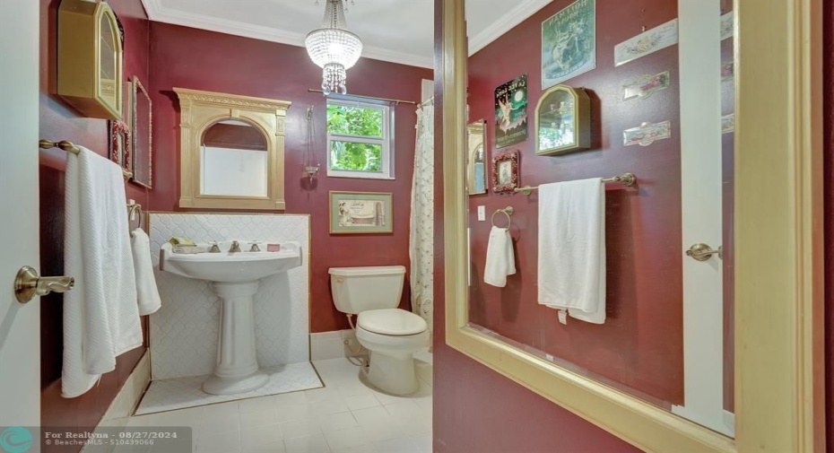 2nd Bathroom, utterly charming, with white pedestal sink frame by custom white tiles, custom hardware, full tub/shower and custom chandelier. Impact glass window too!