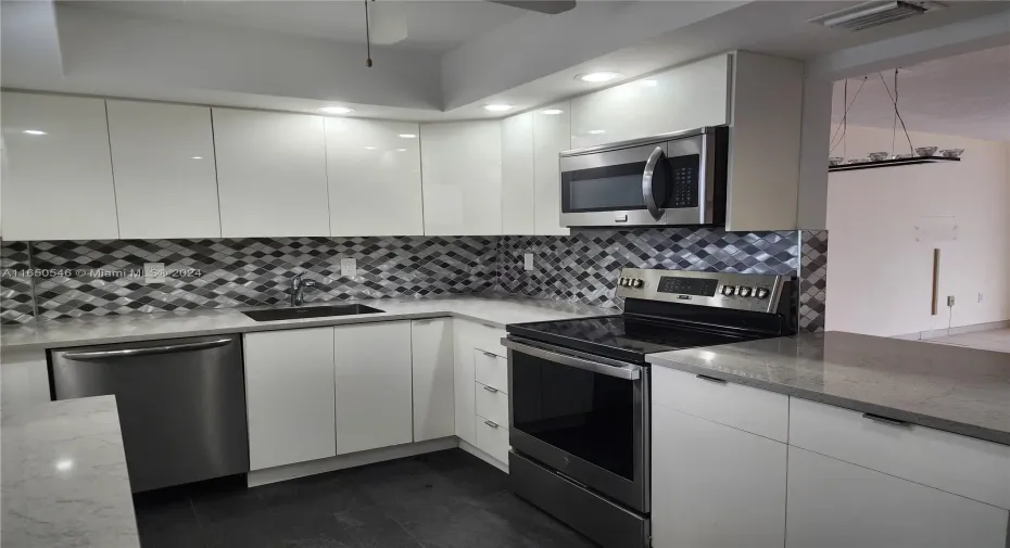 Stainless steel appliances, tile backsplash and tray ceiling with ceiling fan and recessed lighting