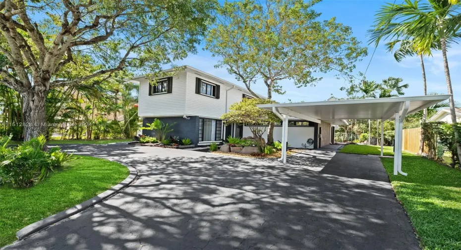 Circular driveway, covered carport & curated tropical landscaping frame the facade of this beautiful Mid-Century Modern residence