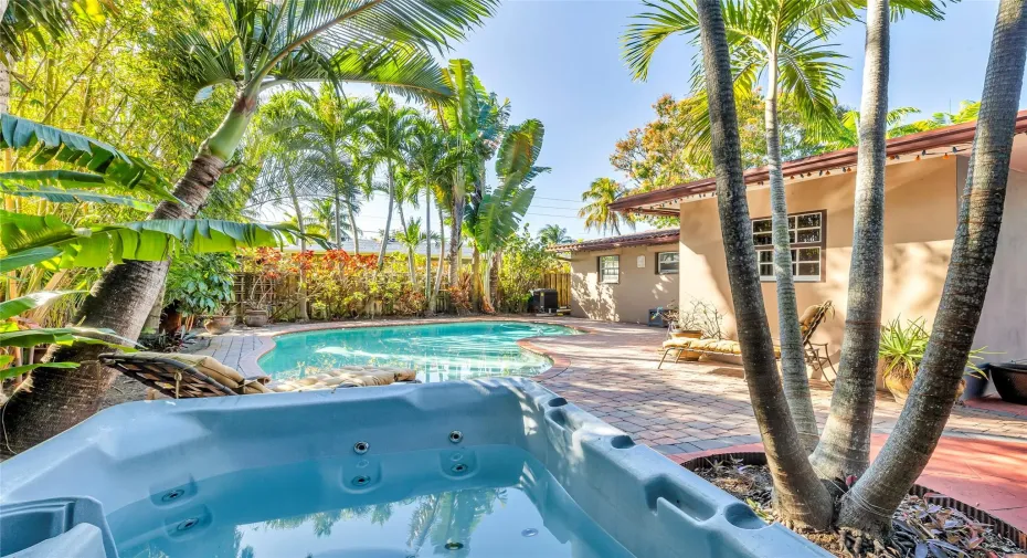 Pool and hot tub and large paver patio surrounded by colorful vegetation.