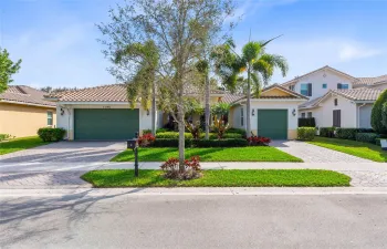 Stunning curb appeal with a lush, tropical landscape featuring vibrant greenery, manicured hedges, and elegant palm trees.